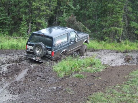 1990 Ford Bronco - Ford Bronco navigating a muddy off-road path with trees in the background.