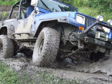 1990 Ford Bronco - A blue Jeep Wrangler navigates a muddy trail, its tires churning through the thick mud.