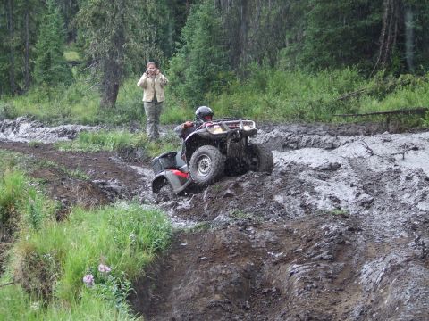 1990 Ford Bronco - An ATV navigates a challenging muddy terrain, with a spectator observing the difficult passage.