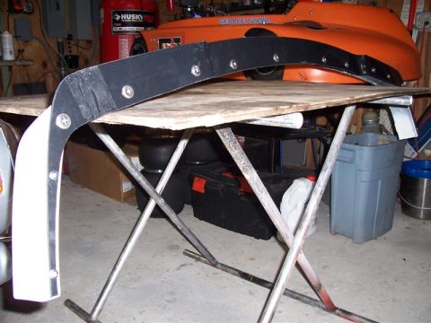 1989 BMW 3 Series - Car fender part on a table, with an orange race car in the background.