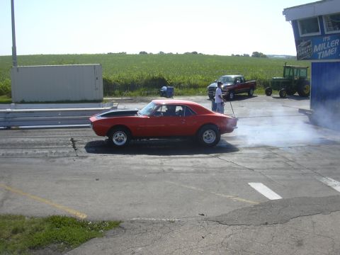 1997 Ford Crown Victoria - A red 1967 Chevrolet Camaro performs a burnout at a drag strip event, with other vehicles visible in the background.