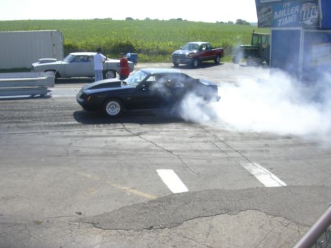1997 Ford Crown Victoria - A black Ford Mustang performs a burnout, creating a large cloud of smoke on the drag strip.