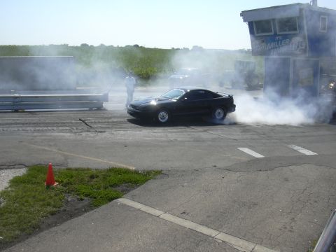 1997 Ford Crown Victoria - A black coupe performs a burnout on a drag strip, surrounded by smoke, with a spectator tower in the background.