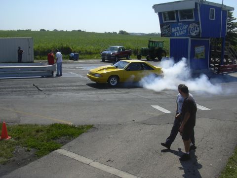 1997 Ford Crown Victoria - A yellow Ford Mustang performs a burnout on the drag strip, creating a large cloud of smoke.