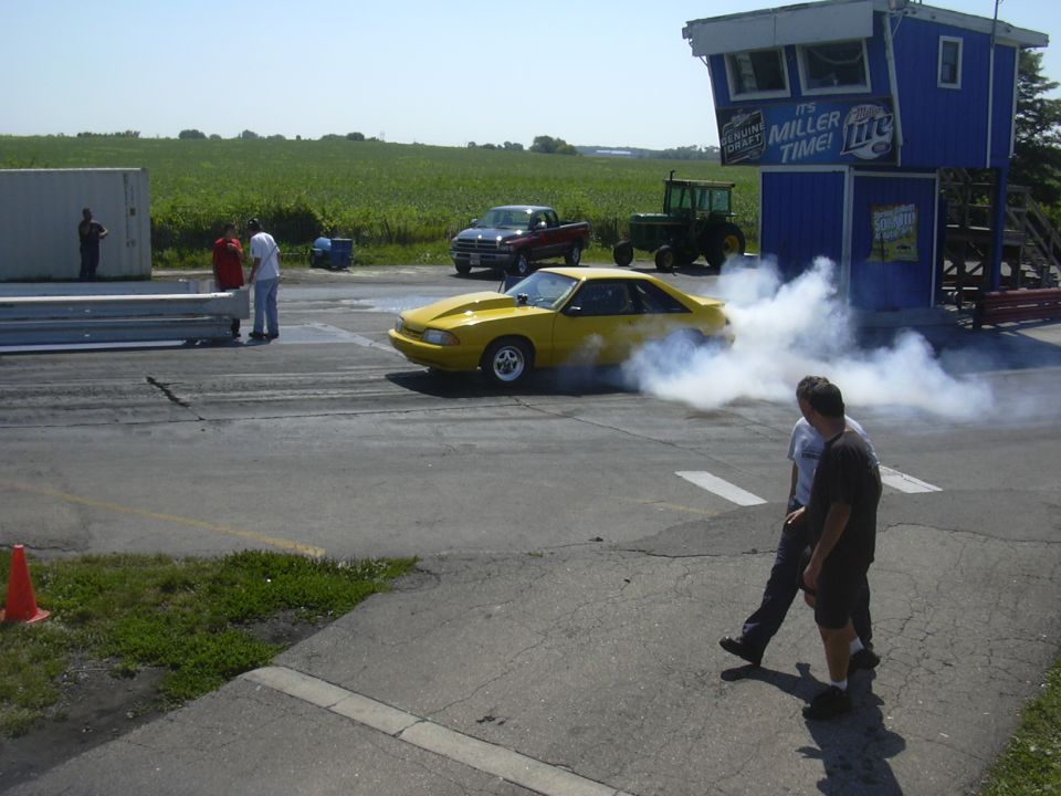 Yellow Ford Mustang doing a burnout on a drag strip