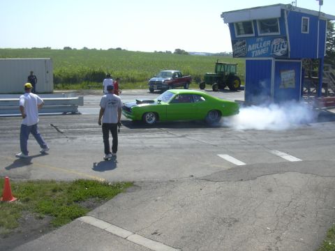 1997 Ford Crown Victoria - A green muscle car performs a burnout on a drag strip, creating a cloud of smoke.