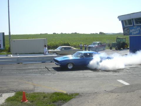 1997 Ford Crown Victoria - Blue muscle car performing a burnout at a drag strip event with other vehicles present.