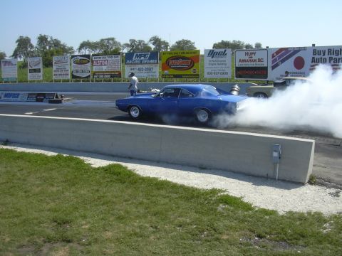 1997 Ford Crown Victoria - A blue muscle car performs a burnout on a drag strip, creating a large cloud of smoke.