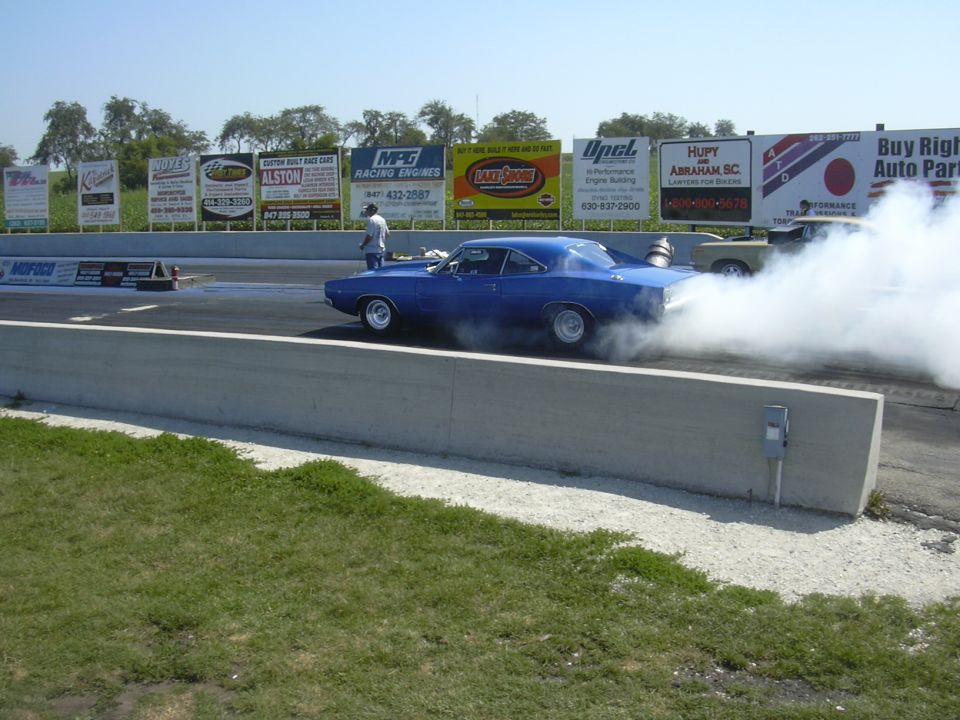 blue muscle car doing a burnout on a drag strip with smoke everywhere