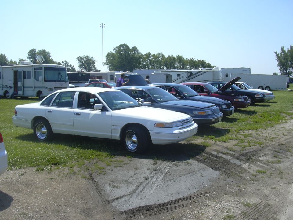 White sedan parked on grass, side view, chrome wheels, some tire marks on dirt