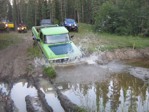 1995 Ford Bronco - Several off-road vehicles navigate a water crossing in a wooded area.