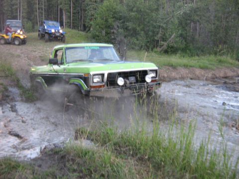 1995 Ford Bronco - A green Ford truck navigates a muddy trail with other off-road vehicles in the background.