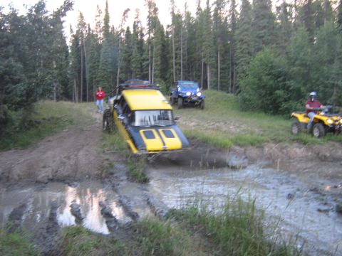 1995 Ford Bronco - Off-road vehicles tackle a muddy trail during an event, with a yellow and black vehicle in the foreground and a blue Jeep and ATV in the ba…