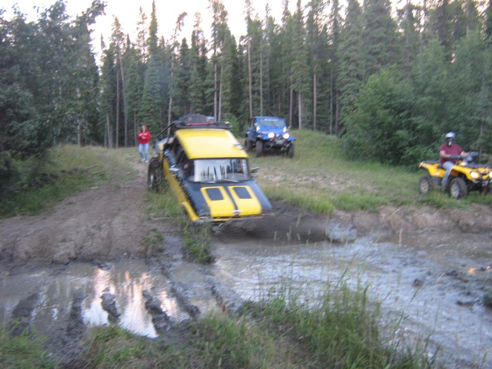Yellow and black off-road vehicle in mud; blue Jeep and yellow ATV in background