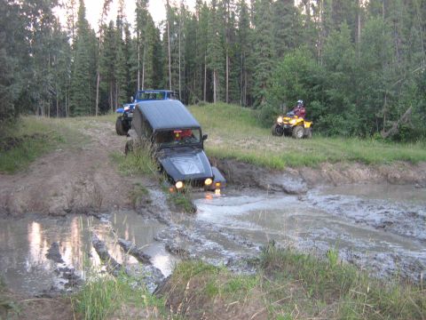 1995 Ford Bronco - Off-road vehicles navigate a muddy trail with trees in the background.