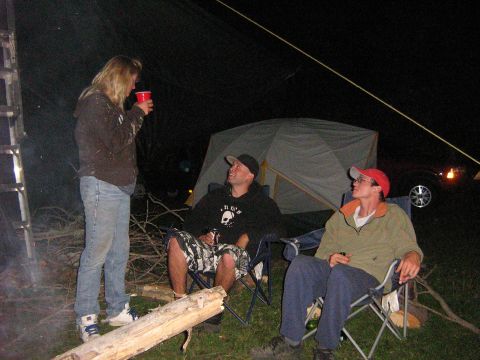 1995 Ford Bronco - A group of people enjoy a nighttime gathering around a campfire, with a tent and a vehicle visible in the dim light.