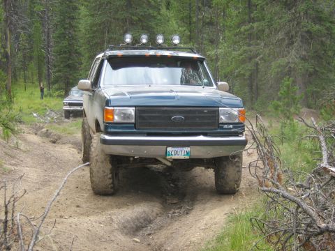 1995 Ford Bronco - Green Ford F-Series truck navigates a muddy trail with another vehicle following in the background.