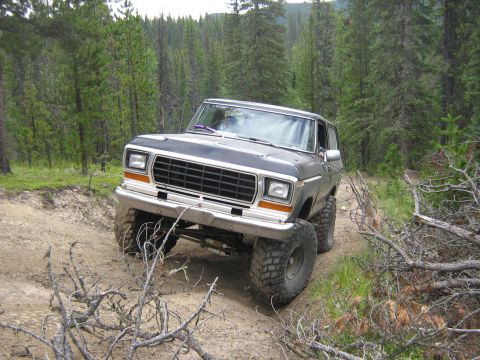 1995 Ford Bronco - A lifted Ford Bronco navigates a wooded trail with steep inclines and loose dirt.