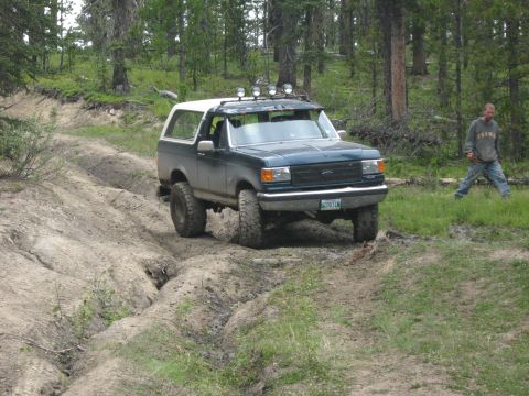 1995 Ford Bronco - A man walks by a Ford Bronco as it navigates a muddy, rutted path through a wooded area.