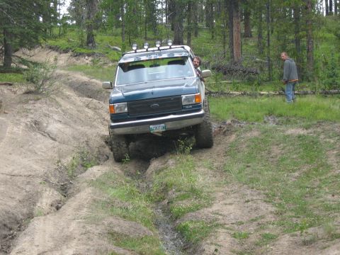 1995 Ford Bronco - A dark green Ford Bronco navigates a challenging dirt trail with a driver visible inside.