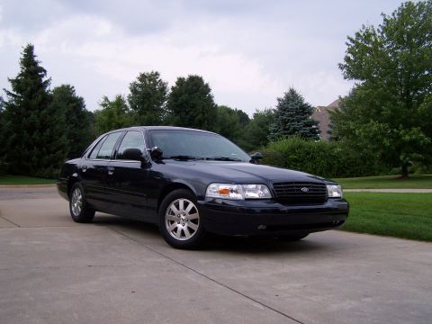 2003 Ford Crown Victoria - This black 2003 Ford Crown Victoria is parked on a concrete driveway with a backdrop of trees and a cloudy sky.