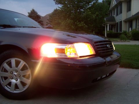 2003 Ford Crown Victoria - Front corner view of a dark blue 2003 Ford Crown Victoria with its headlights illuminated.