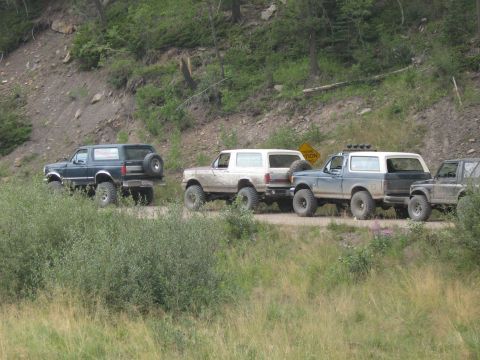 1995 Ford Bronco - A line of Ford Broncos travels down a dusty mountain road, kicking up dust as they go.