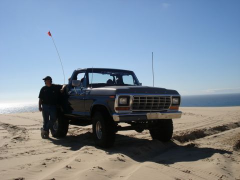 1979 Ford Bronco - A man stands next to a lifted 1979 Ford Bronco on a sandy beach with the ocean visible behind it.