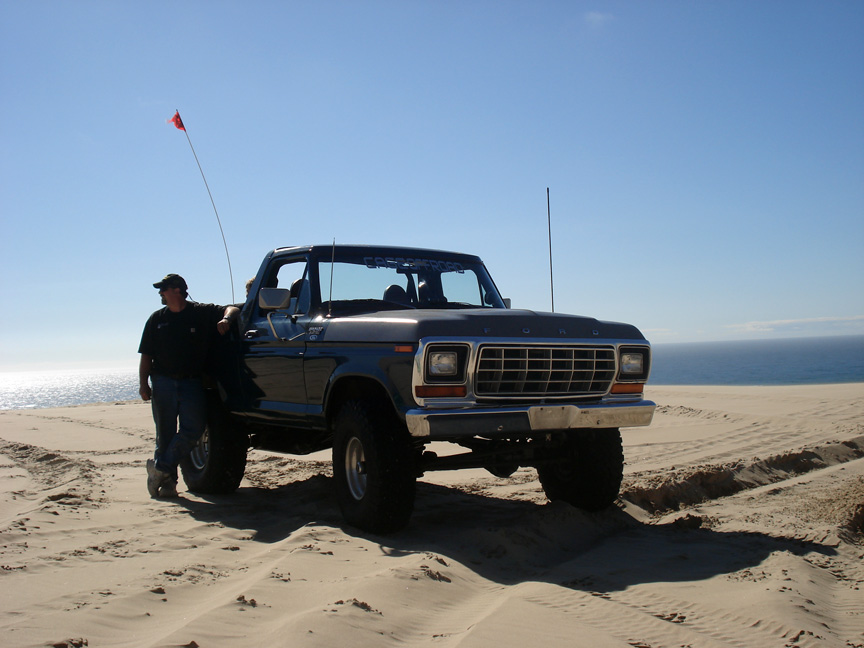 Gray 1979 Ford Bronco on sand dunes with ocean in background