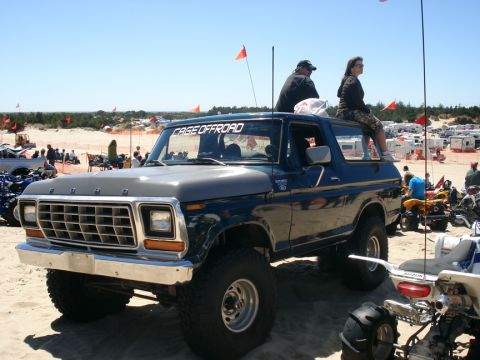 1979 Ford Bronco - This lifted Ford Bronco is parked on the sand with people relaxing on its roof and other off-road vehicles nearby.