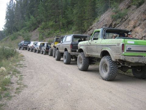 1995 Ford Bronco - A line of modified Ford Broncos drives down a dusty mountain road.