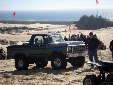 1979 Ford Bronco - A lifted 1979 Ford Bronco is parked on a sandy dune, with the ocean and other off-road vehicles visible in the background.
