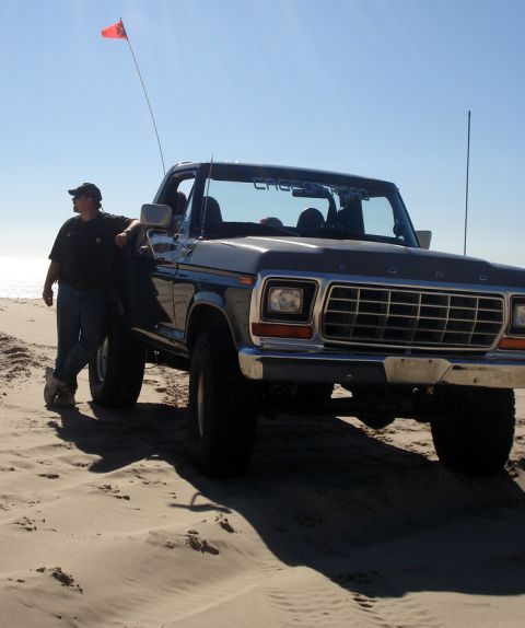 1979 Ford Bronco - Man and his 1978 Ford Bronco parked on a sandy beach under a clear blue sky.
