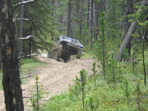 1995 Ford Bronco - A 4x4 vehicle navigates a challenging off-road trail through a dense forest.