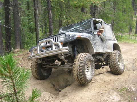 1995 Ford Bronco - Modified Jeep Wrangler tackling an off-road trail with large mud-terrain tires.