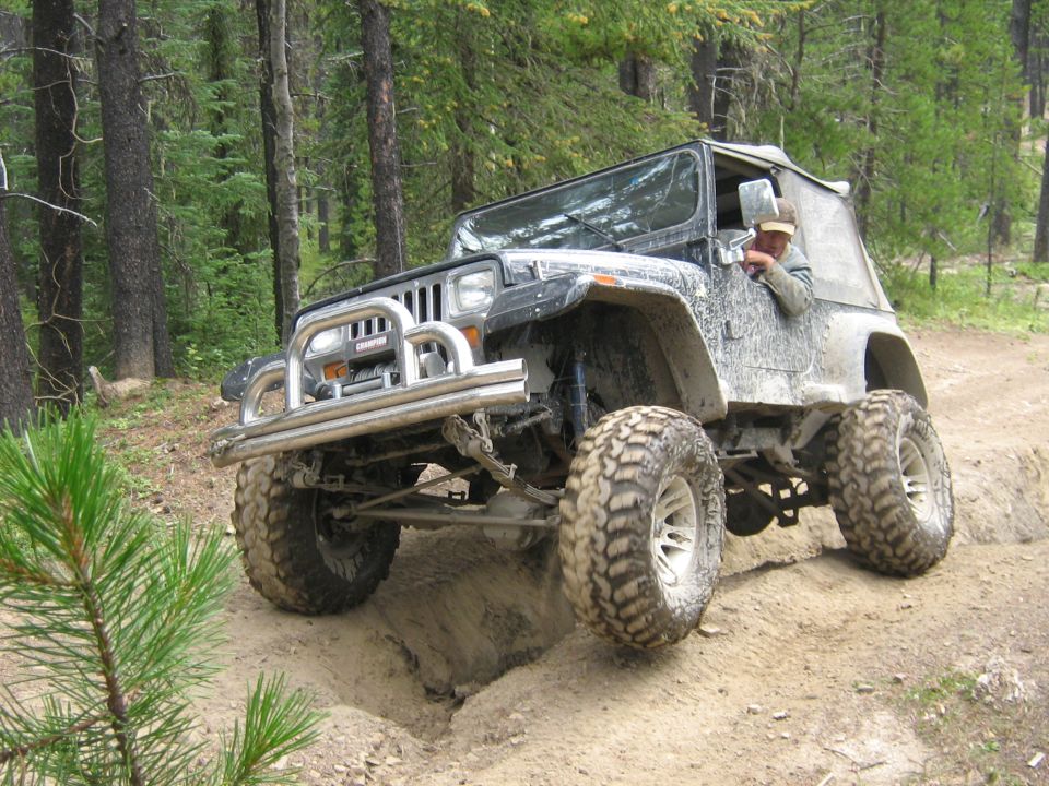 Jeep Wrangler with large tires navigating a dirt trail in a forest