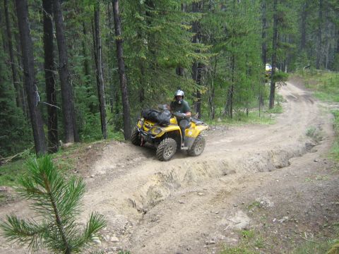 1995 Ford Bronco - An ATV navigates a challenging dirt path through a wooded area, with another vehicle in the distance.