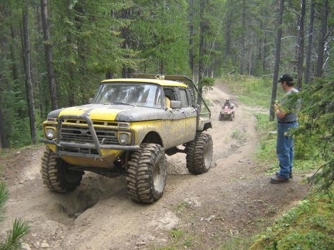 1995 Ford Bronco - A heavily modified truck navigates a wooded trail with an ATV in the distance.