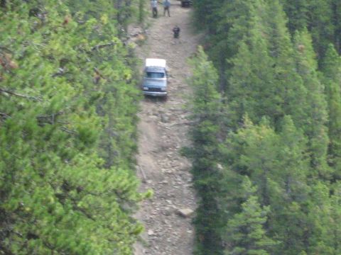 1995 Ford Bronco - A van navigates a challenging dirt road in a wooded area, with several people walking ahead.