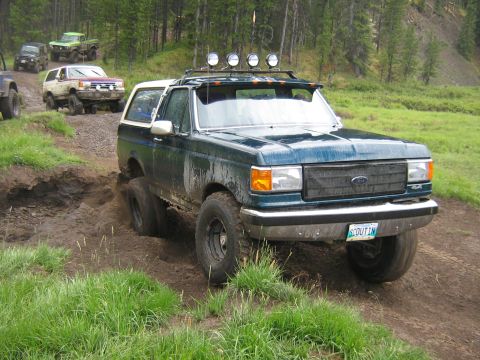 1995 Ford Bronco - Multiple off-road vehicles navigate a muddy trail during an event.