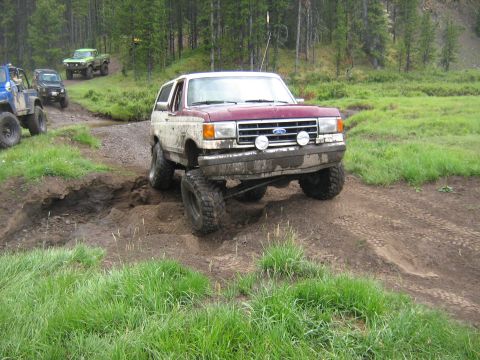1995 Ford Bronco - Several off-road vehicles are seen navigating a muddy trail through a wooded area.