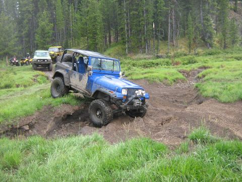 1995 Ford Bronco - Several off-road vehicles, including a blue Jeep Wrangler, traverse a muddy track in a wooded area.