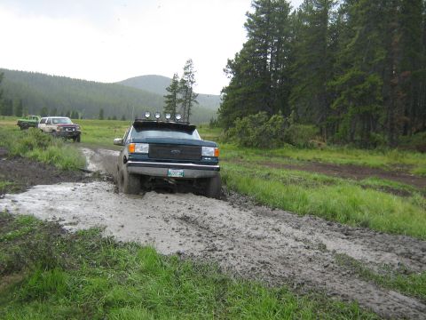 1995 Ford Bronco - A Ford truck navigates a muddy trail with other vehicles in the distance.