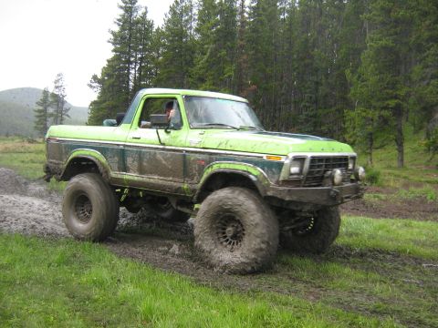 1995 Ford Bronco - A modified Ford Bronco navigates a muddy off-road course with trees in the background.
