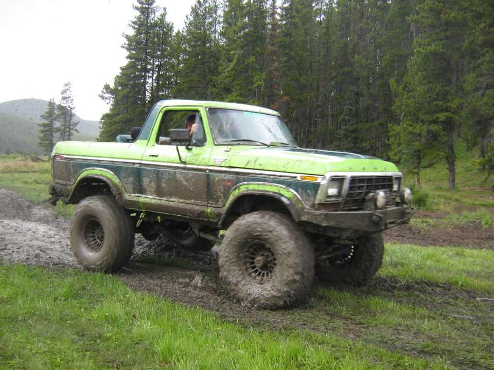 Green Ford Bronco with large tires driving through mud and grass