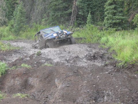 1995 Ford Bronco - An off-road vehicle navigates a challenging muddy terrain in a wooded area.