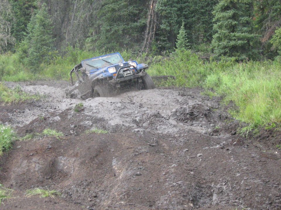Blue off-road vehicle with winch stuck in deep mud on a wooded trail