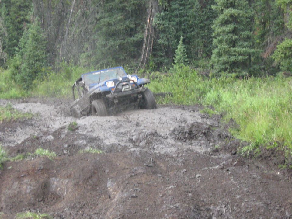 Blue off-road vehicle stuck in mud with trees in background