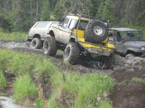 1995 Ford Bronco - Several off-road vehicles navigate a muddy trail during an event.