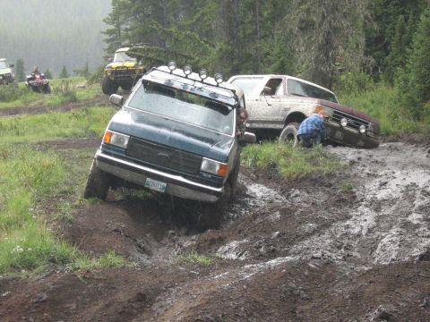 1995 Ford Bronco - Multiple off-road vehicles struggle on a wet, muddy track during an event.
